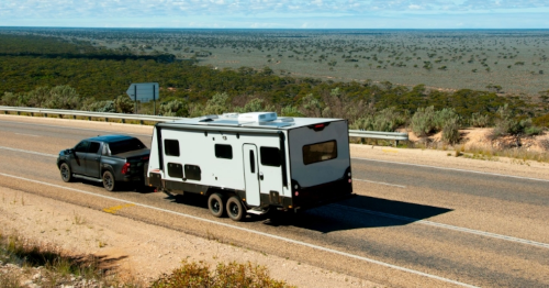 Black truck towing a camper on a desert highway under a clear sky.